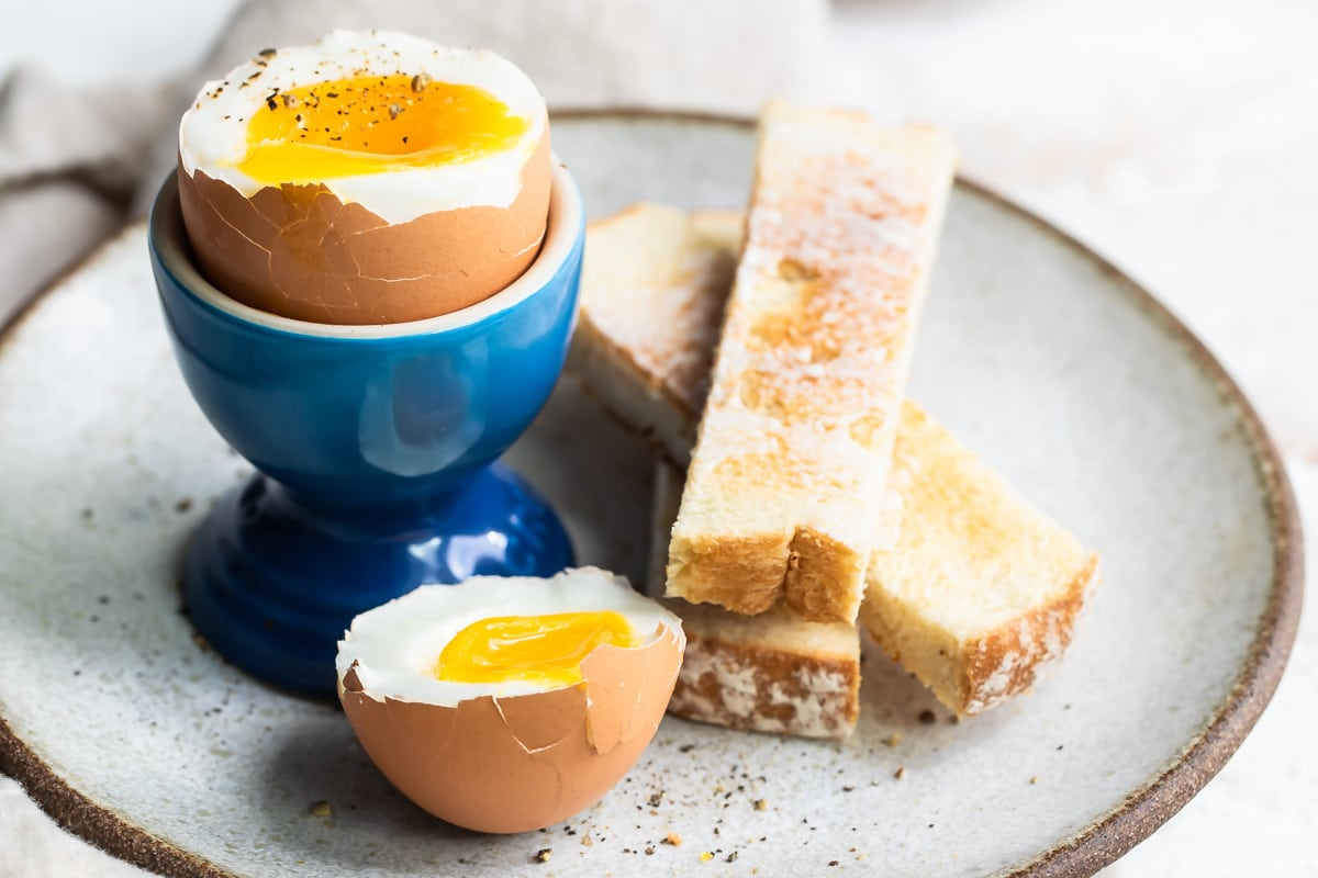 Um ovo cozido macio em um copo de ovo azul com torradas ao lado.