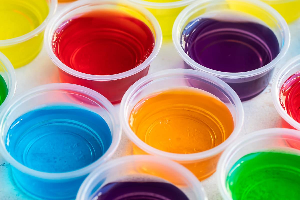 Vários shots de gelatina colorida em copos de porções claras.