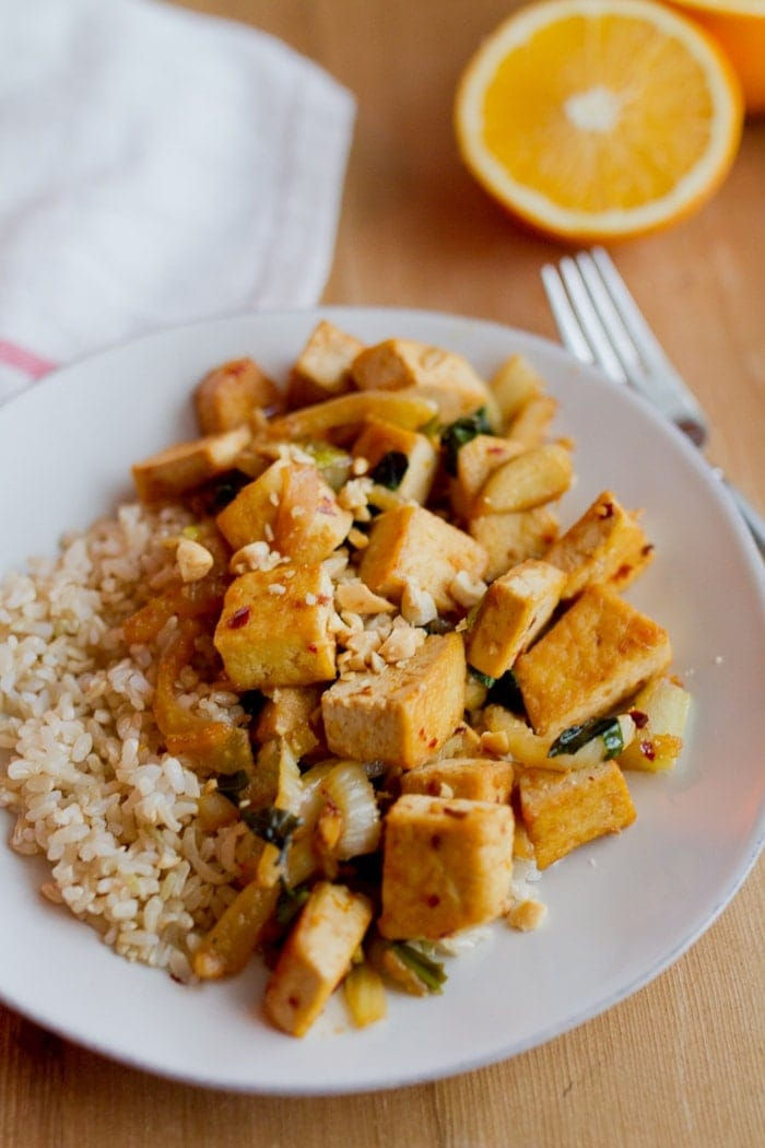 Tofu de tofu laranja frito com funcho e servido sobre arroz marrom no prato branco.