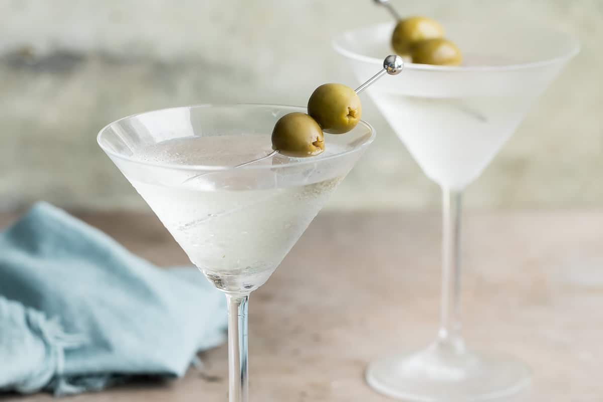 Dois martinis secos guarnecidos com azeitonas verdes.