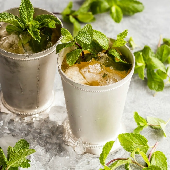 Dois Juleps de menta em copos de prata rodeados de gelo e ramos de menta.