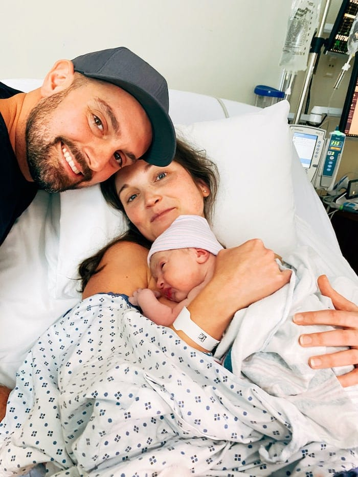 Um casal a sorrir e a segurar a bebé recém-nascida no hospital.