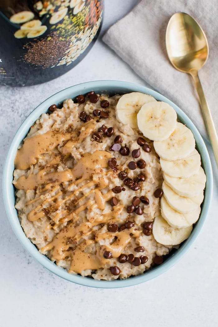 Aveia coberta com manteiga de aveia chuviscada, pedaços de chocolate e banana fatiada. Colher na lateral.