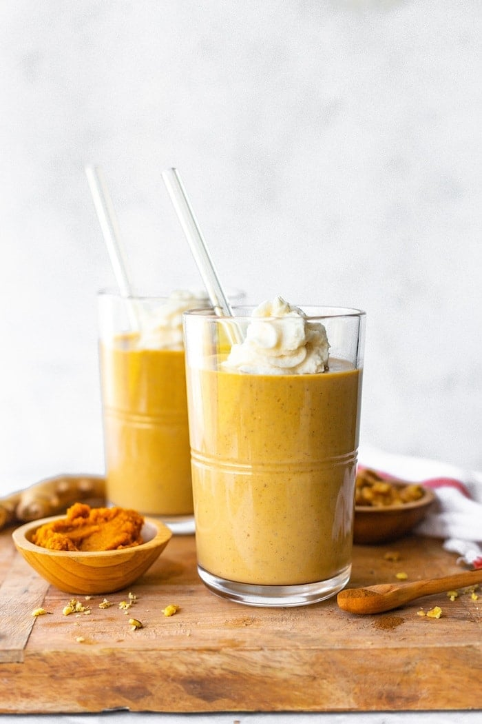 Dois smoothies de gengibre de abóbora sobre uma tábua de madeira coberta com chantilly.