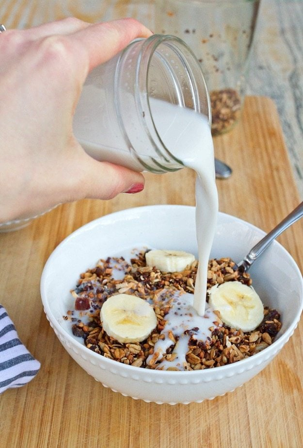 Cereal caseiro sem Glúten com Quinoa Buckwheat & Dates em uma tigela com leite sendo derramado na tigela a partir de um frasco de pedreiro.