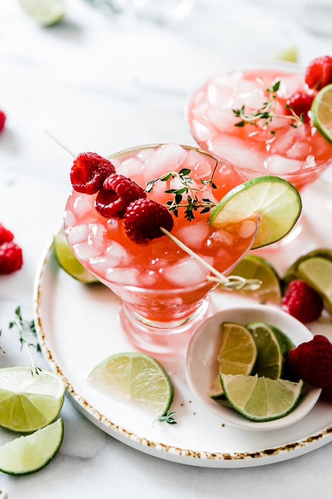 Raspberry Limeade caseiro em copos de martini, rodeado por fatias de lima.