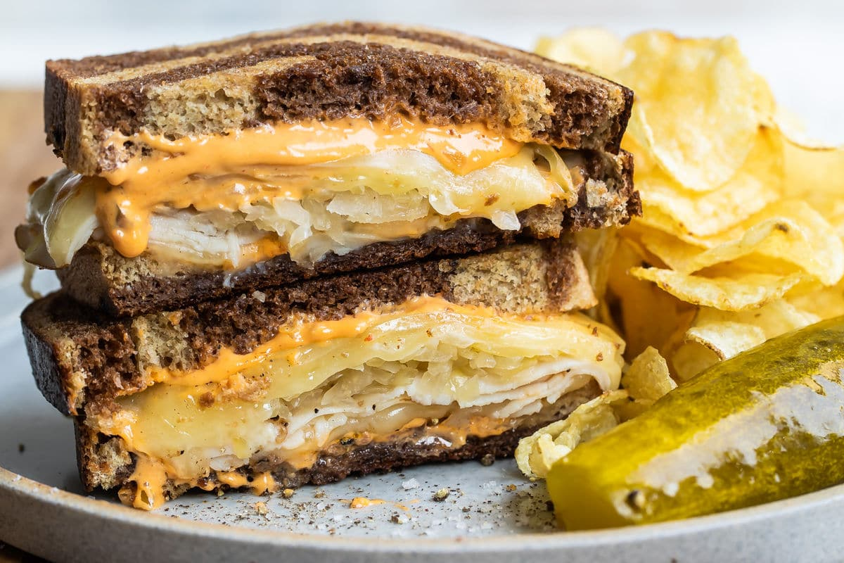 Um sanduíche de rachel num prato cinzento com uma lança de picles e batatas fritas.
