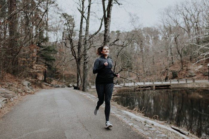 Mulher a correr numa estrada junto a um lago com todo o desgaste atlético negro.