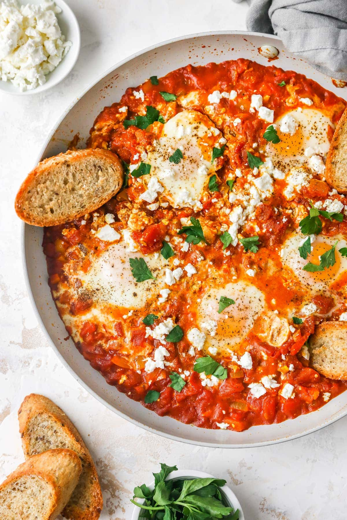 Shakshuka cozida em uma panela salteada com ervas frescas, feta e uma fatia de pão estaladiço.