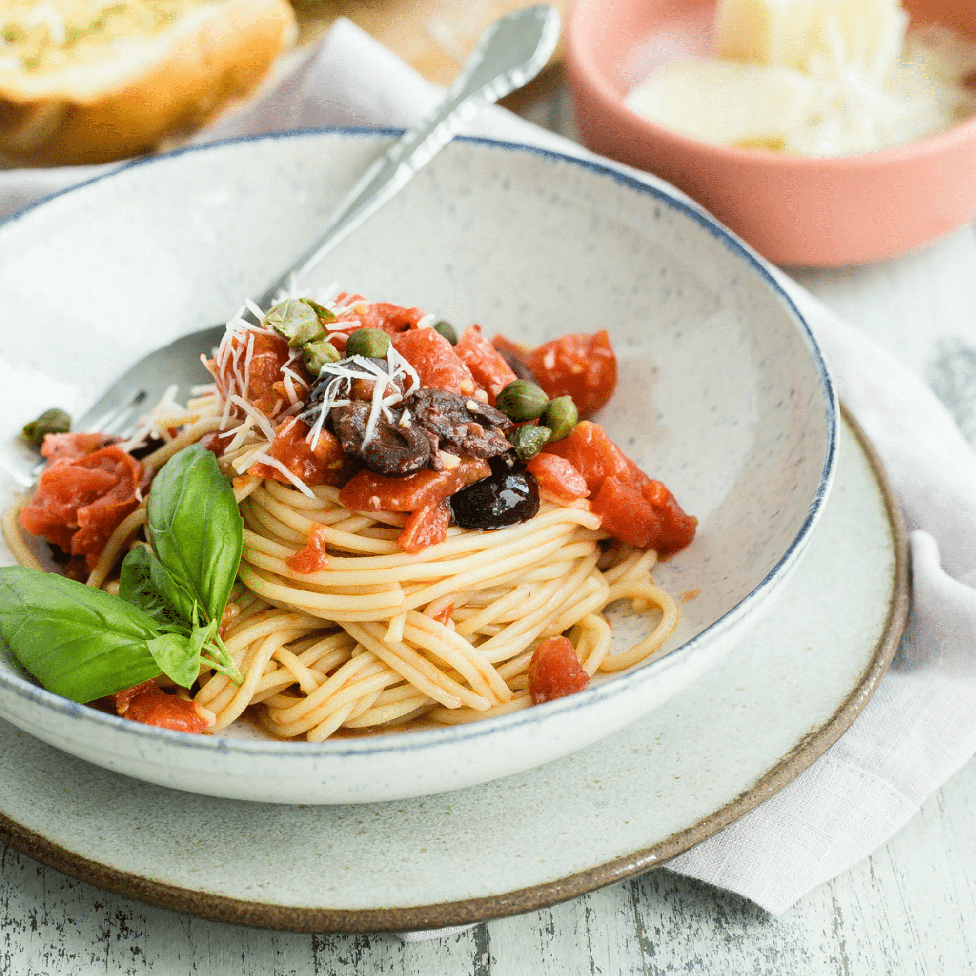 Spaghetti alla Puttanesca numa tigela branca com garfo de prata.