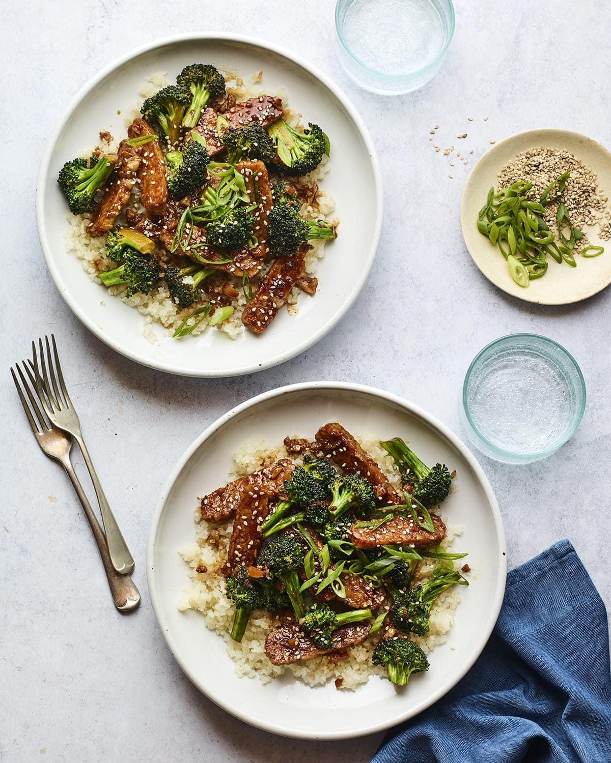 Dois pratos de teriyaki tempeh e brócolos servidos sobre o arroz.