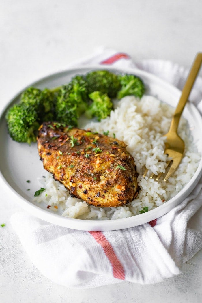 Frango com caril grelhado num prato com arroz e brócolos.