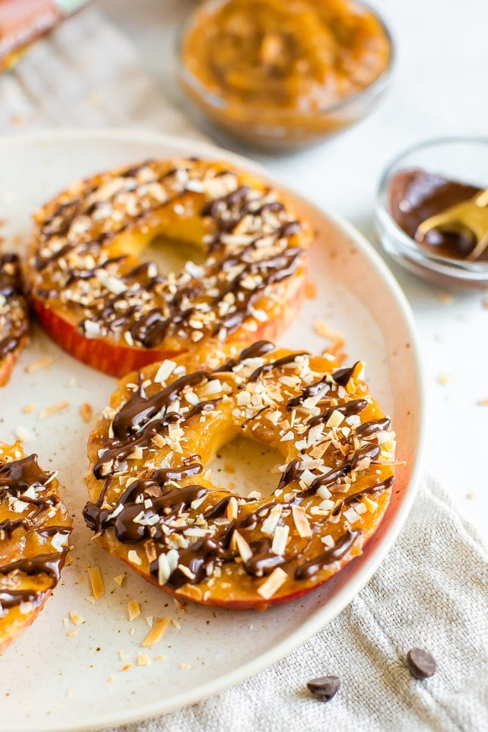 Samoas de maçã num prato. Anéis de maçã cobertos com caramelo, chuvisco de chocolate e flocos de coco.