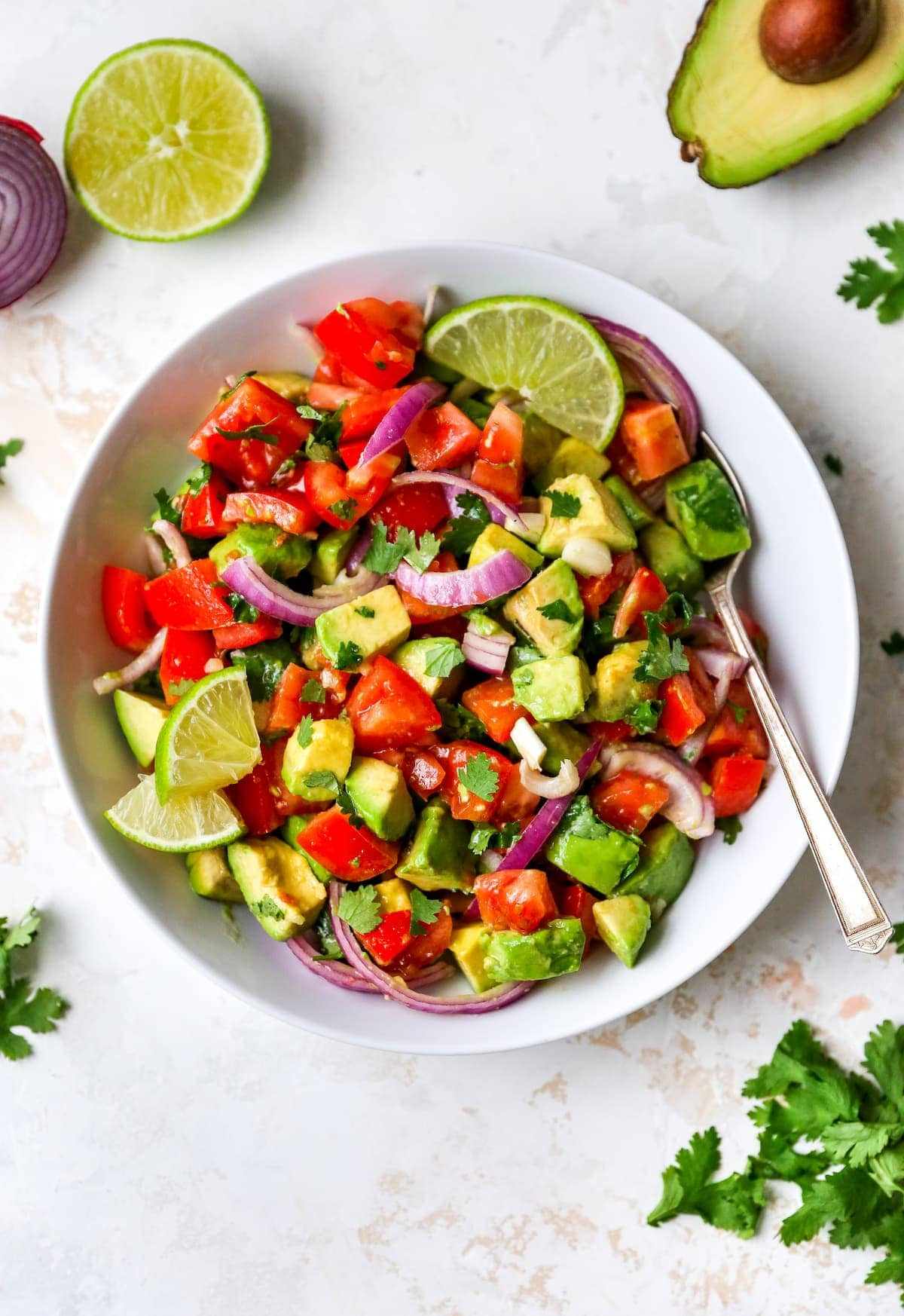 Tigela para servir com abacate e salada de tomate guarnecida com limão e coentro. Uma colher está na tigela.