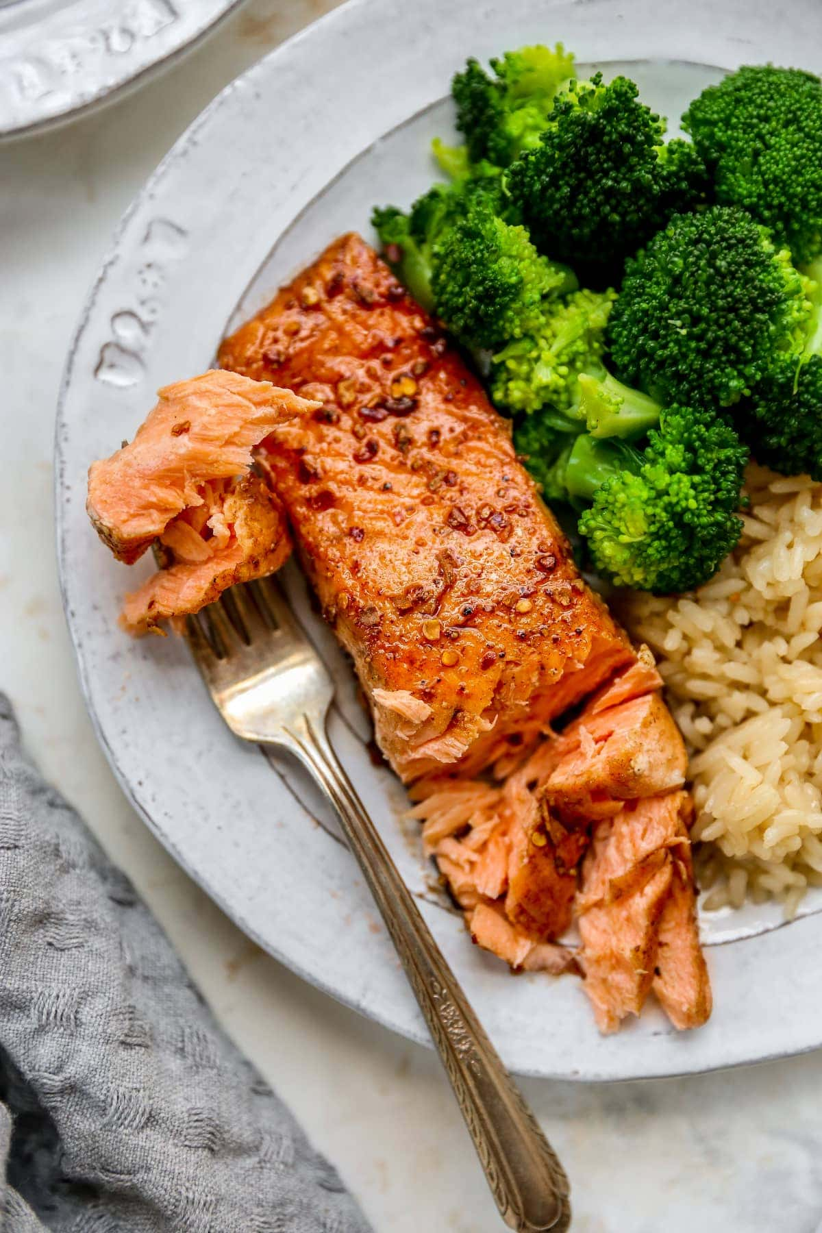 Prato com um pedaço de salmão balsâmico, arroz integral e brócolos. O garfo está a dar uma dentada no salmão.