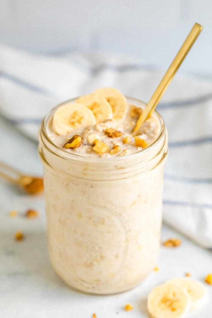 Frasco de pedreiro com pão de banana para passar a noite, coberto com fatias de banana e nozes. O frasco de pedreiro tem um cabo de colher de ouro a sair.