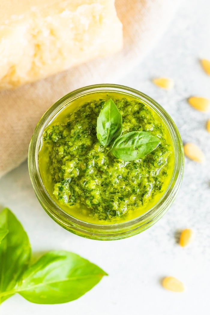 Foto aérea de um frasco de vidro cheio de pesto caseiro com folhas de manjericão fresco na parte superior.