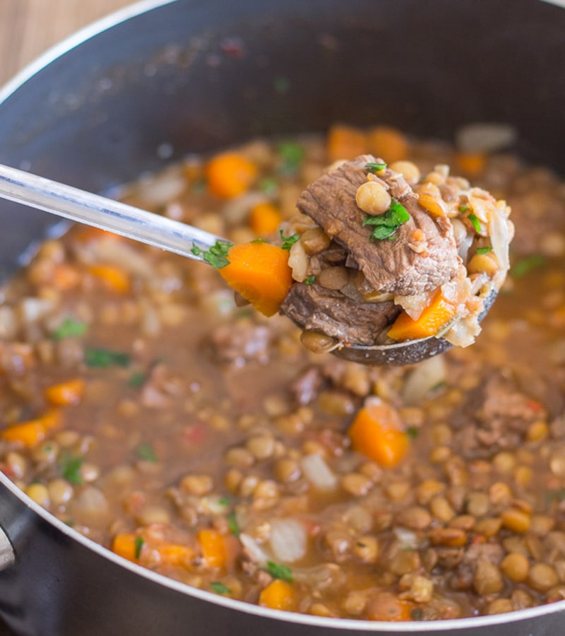 Sopa de carne e lentilhas numa panela com algumas numa concha.