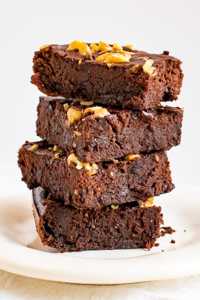 Pilha de brownies de feijão sem farinha, cobertos com pepitas de chocolate e nozes.