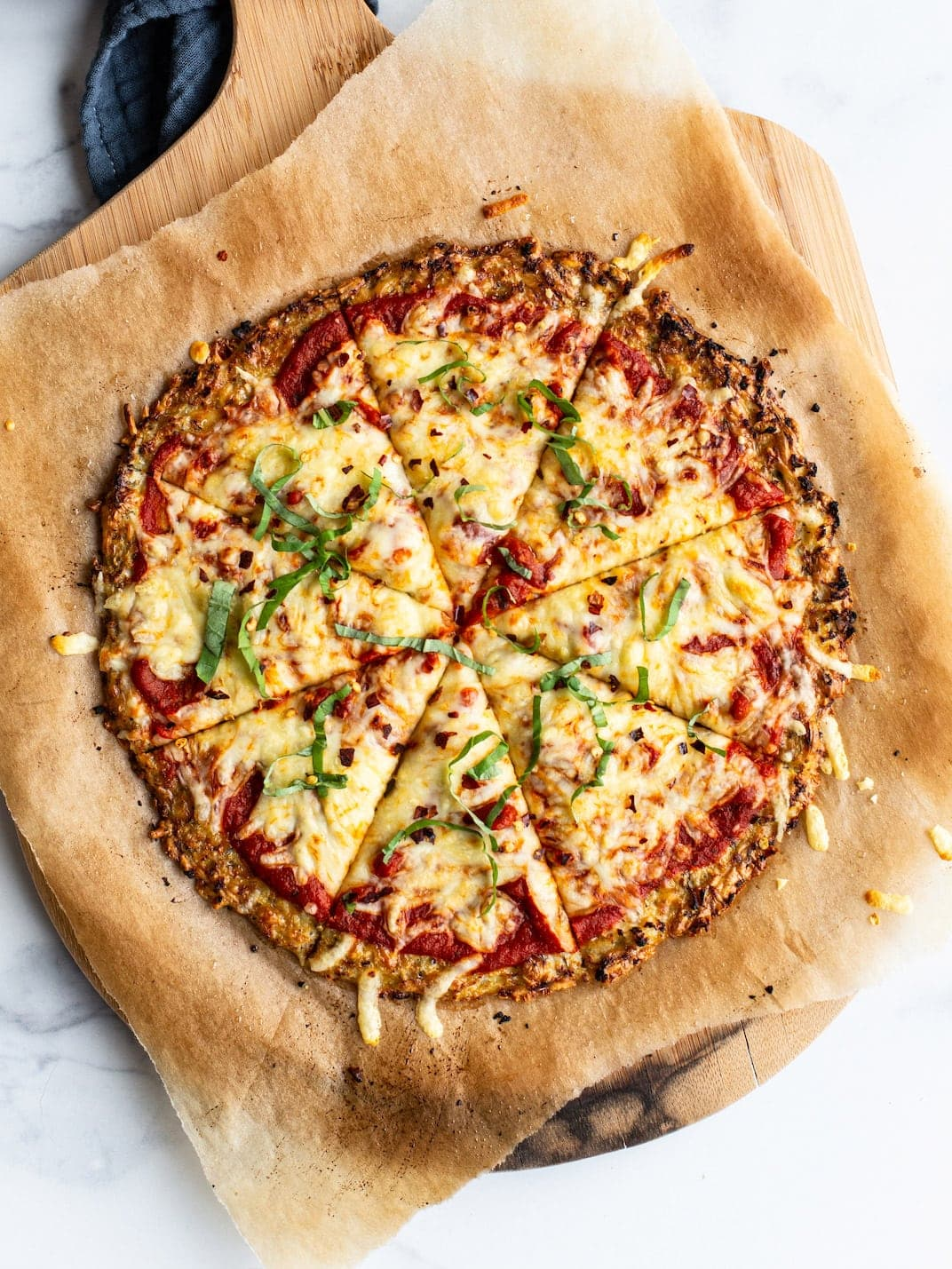 Pizza de couve-flor em papel pergaminho e uma pá de pizza de madeira.