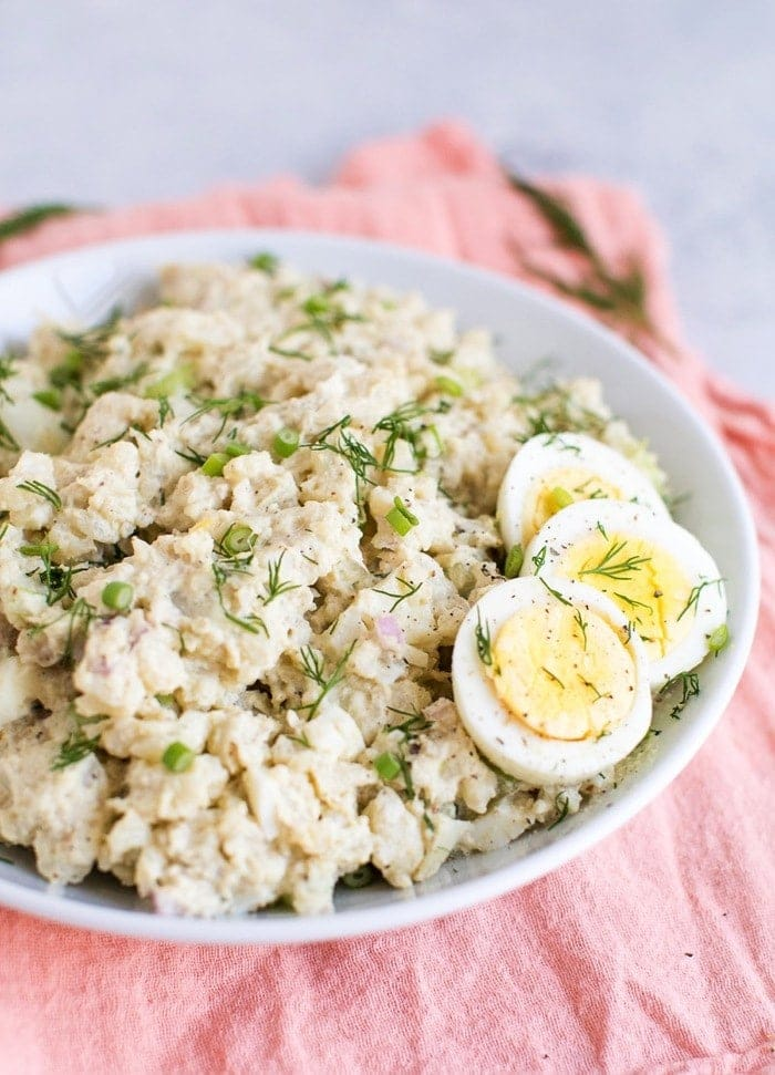 Salada de batata couve-flor numa tigela branca com três fatias de ovo cozido na lateral.