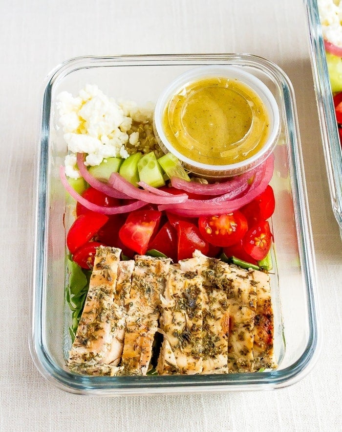 Recipiente de preparação de refeição em vidro com tomate de frango grelhado, cebola em conserva, pepino, quinoa, verduras, feta e vinagrete de limão.