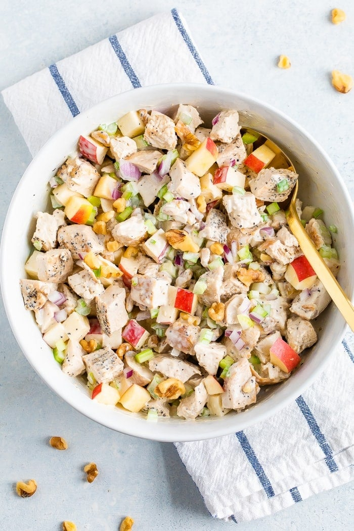 Tigela de salada Waldorf de frango feita com pedaços de frango grelhado, maçã picada, aipo, cebola, ervas aromáticas, nozes e um molho cremoso.