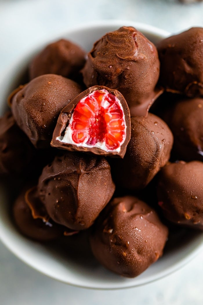 Tigela de framboesas congeladas cobertas de chocolate com iogurte. Uma framboesa é cortada ao meio.