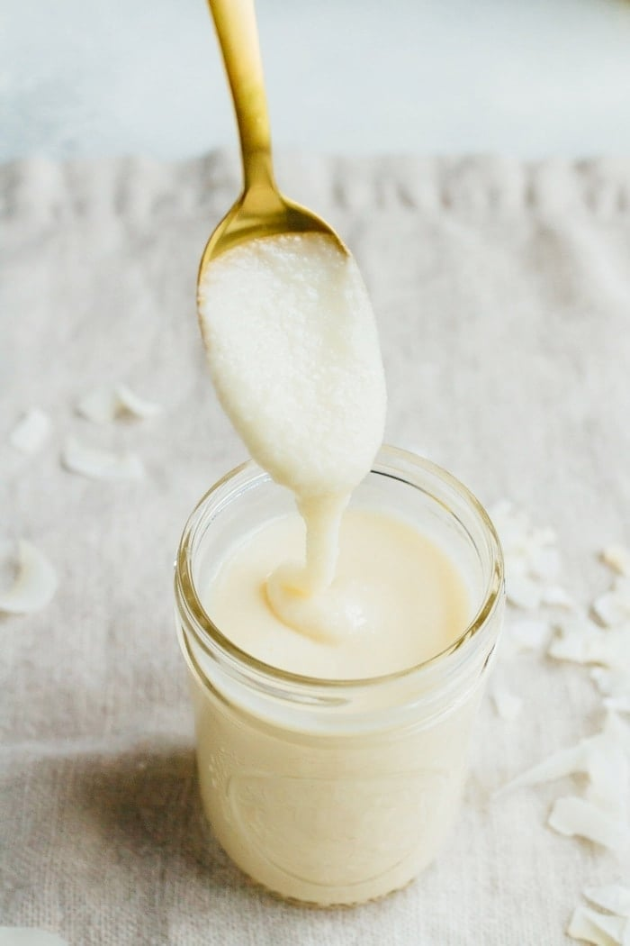 Manteiga de coco num pequeno frasco de pedreiro com uma colher cheia numa colher de ouro.
