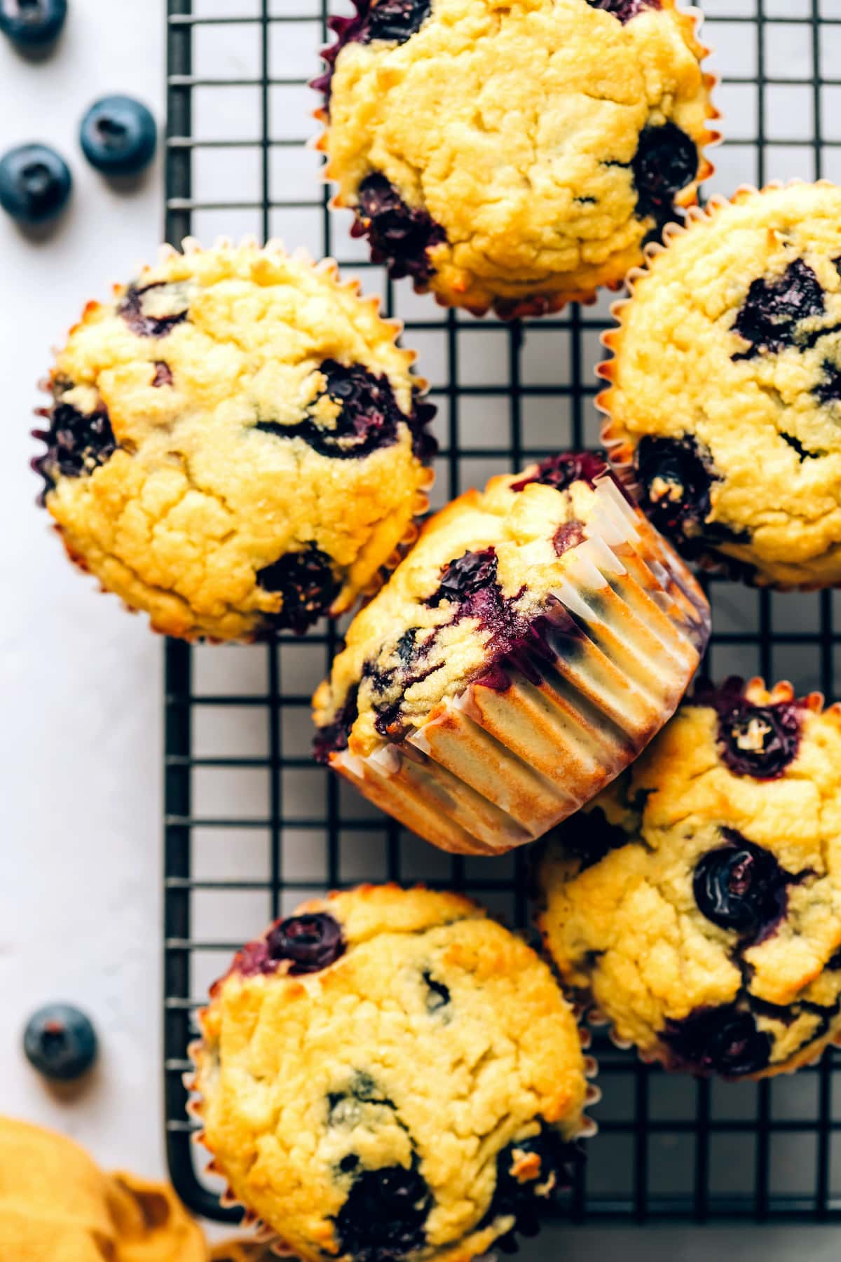 Uma vista aérea dos muffins de farinha de coco dispostos em uma grade de resfriamento de arame. Um muffin é virado de lado.