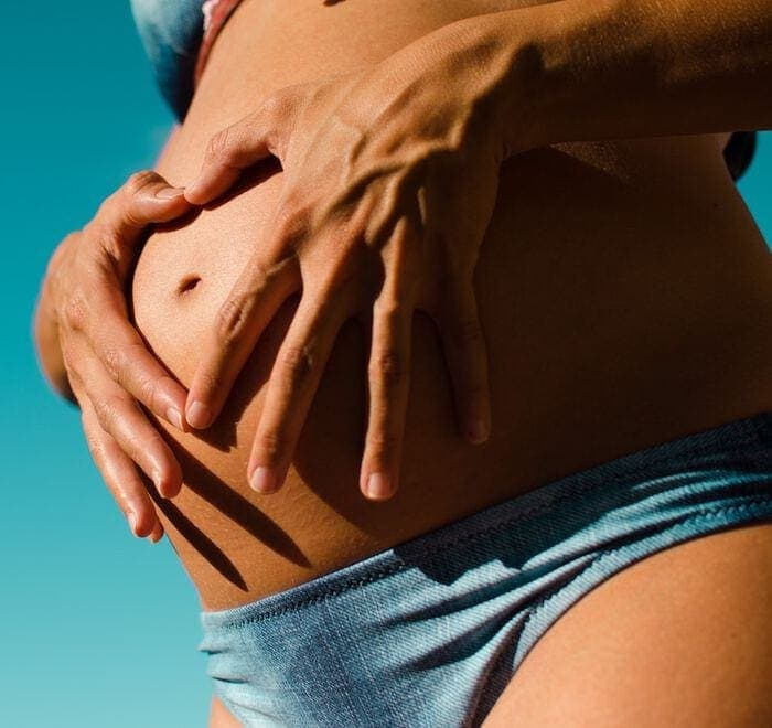 Mulher grávida vestindo um biquíni azul e segurando o estômago.