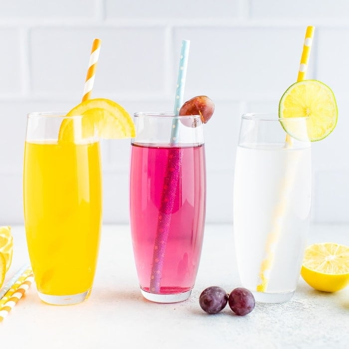 Três copos de refrigerante caseiro de sabor diferente com palhinhas de papel.