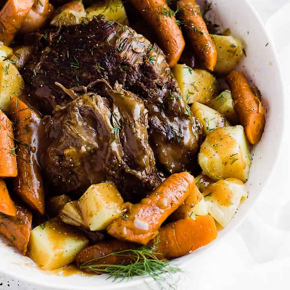 Carne assada congelada numa tigela rodeada de cenouras e batatas.