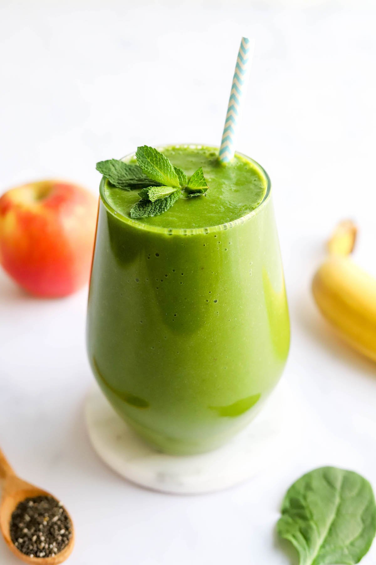 Um copo contendo smoothie verde de desintoxicação coberto com um raminho de menta fresca e uma palha listrada.