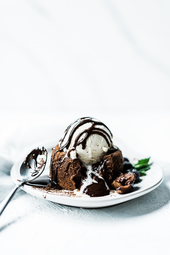 Receita de bolo de chocolate derretido em um prato branco, guarnecido com sorvete de baunilha e mirtilos.