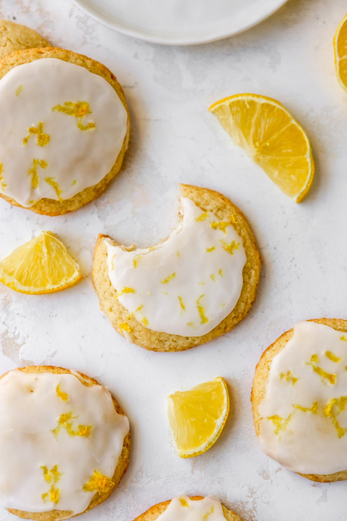 Uma foto aérea olhando para biscoitos de farinha de amêndoa limão espalhados em cima de uma mesa. O biscoito central tem uma dentada removida.