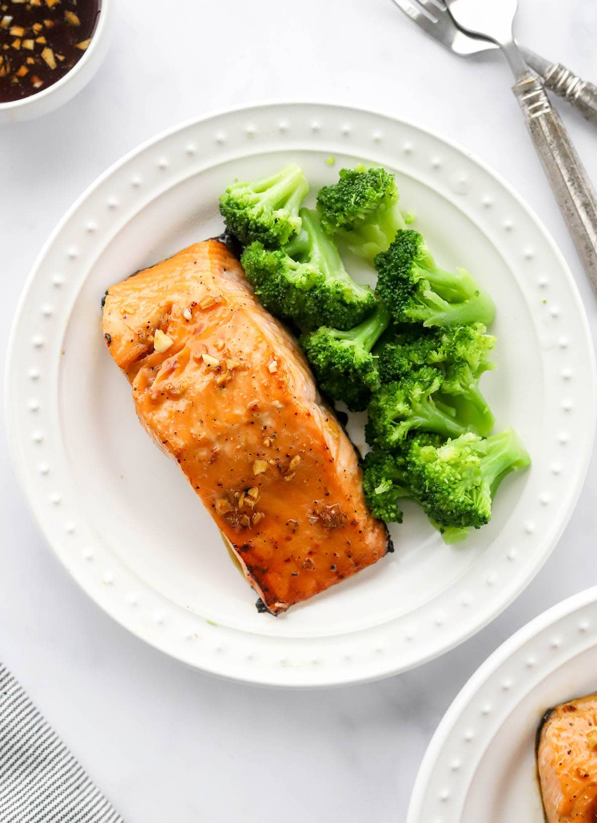 Uma foto aérea de um prato com um filete de salmão de bordo vidrado. Os brócolos cozidos a vapor também estão no prato.