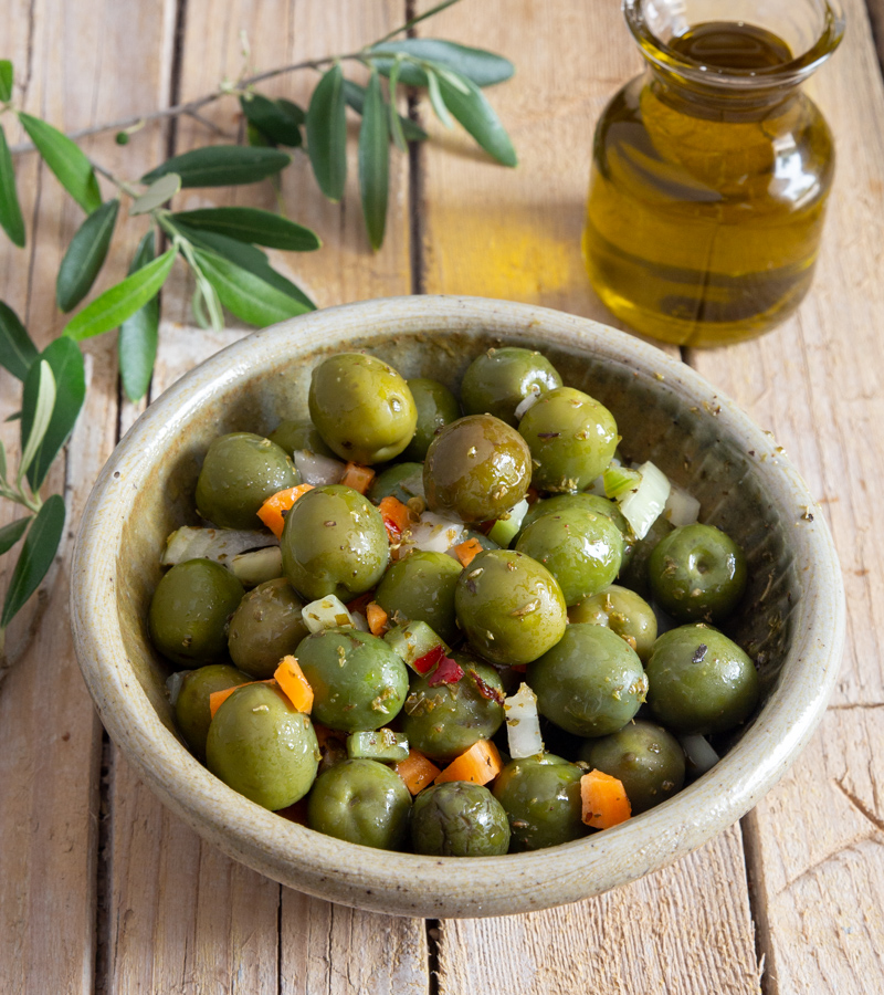 Salada de azeitonas verdes numa tigela cinzenta e azeite de oliva num frasco de vidro.