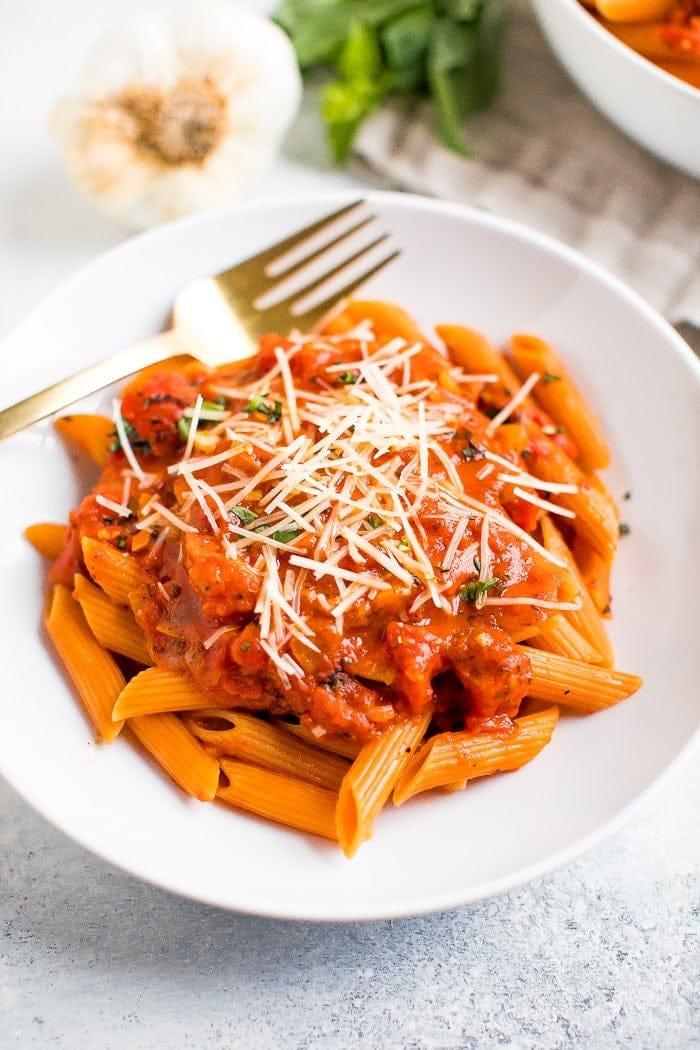 Penne saudável e vegetariana à vodka num prato ao lado de alho e manjericão fresco.