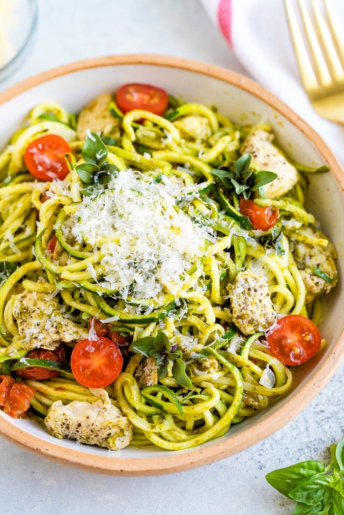 Tigela de cerâmica com massa de abobrinha pesto com frango e tomate cereja, coberta com parmesão.