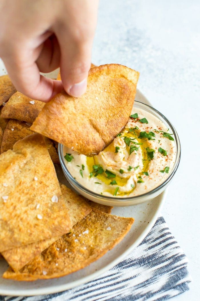 Mergulhar à mão um chip pita numa tigela de hummus.