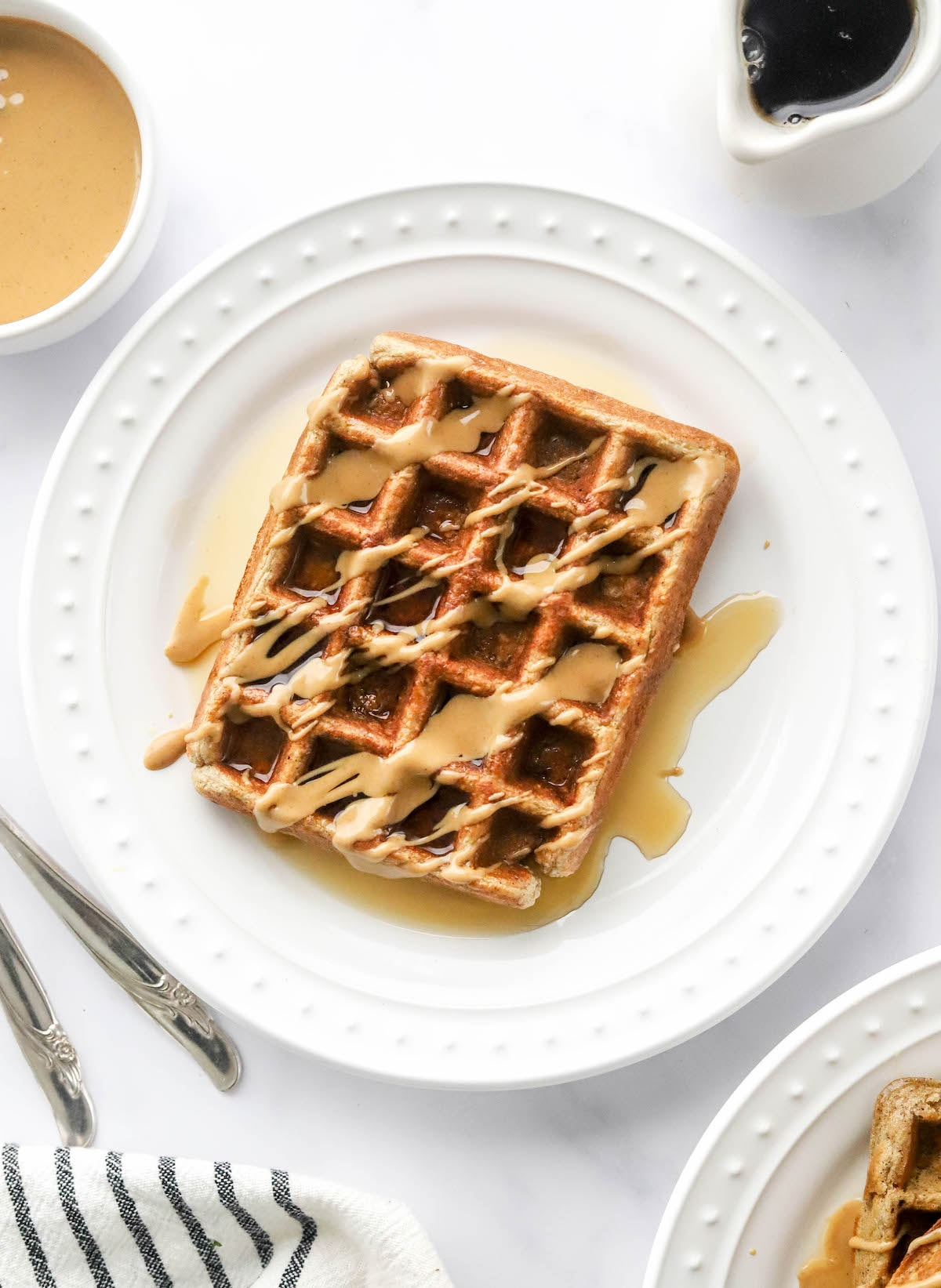 Uma foto aérea olhando para um prato com um waffle de proteína retangular que foi regado com xarope de ácer e manteiga de amendoim.