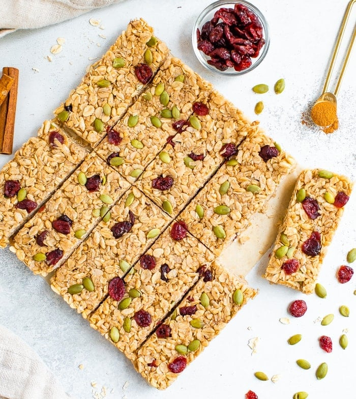 Barras de granola com especiarias de abóbora em uma mesa rodeada de pepitas, arandos e canela.