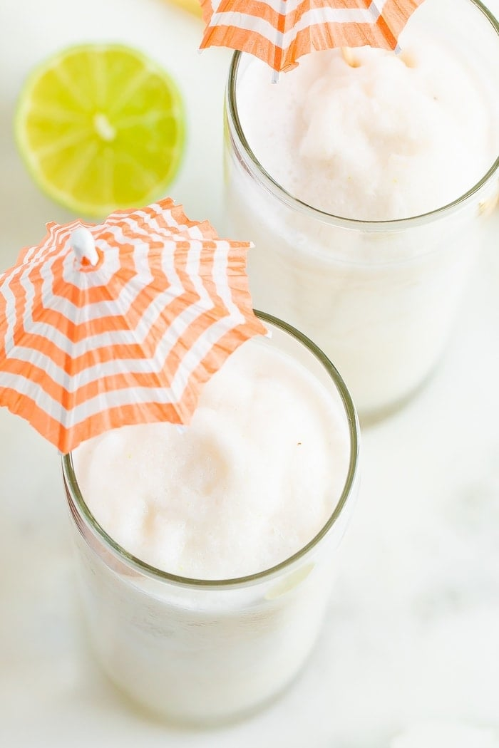 Feche a foto aérea com dois coquetéis daiquiri de coco magro em copos altos com guarda-chuvas de laranja e riscas brancas.