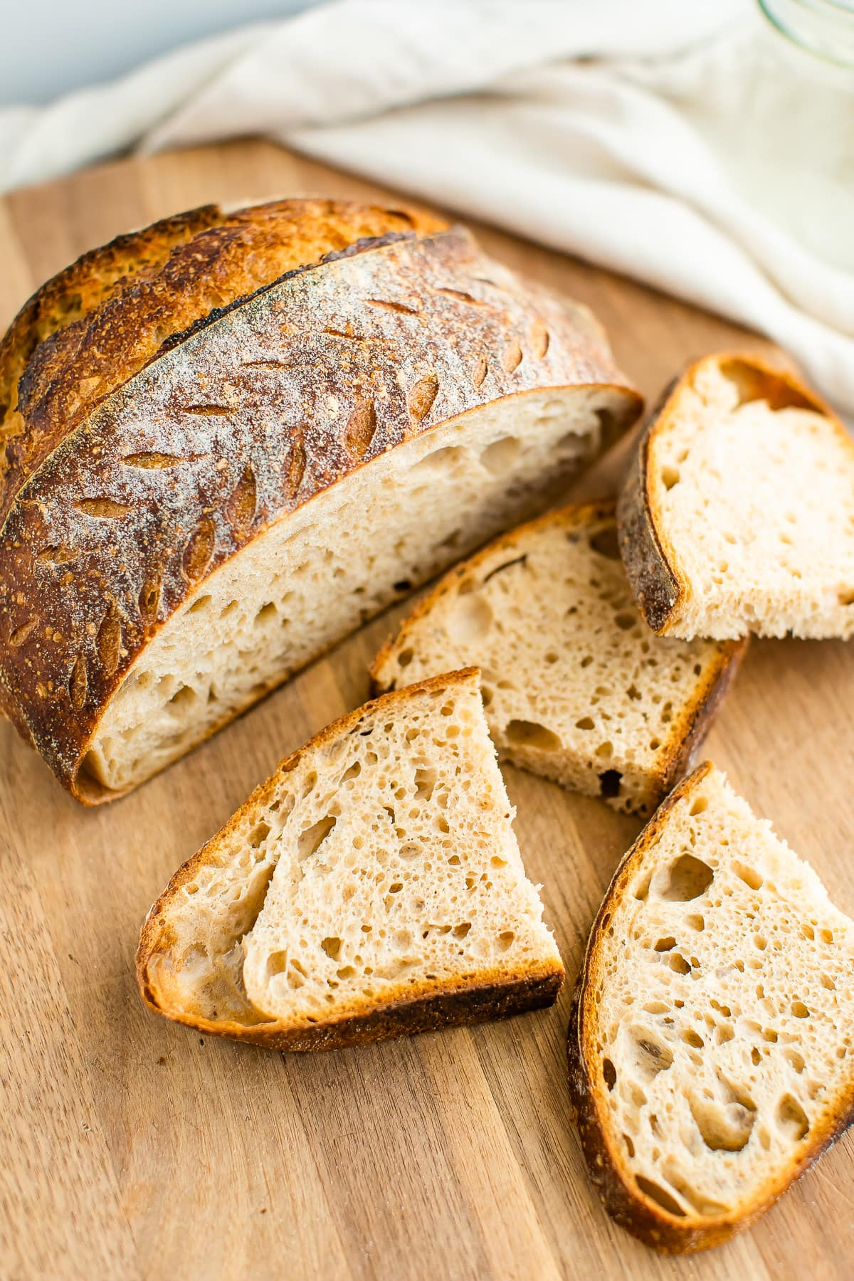 Um pão de massa de pão aberto em fatias sobre uma tábua de madeira com 2 fatias cortadas ao meio, espalhadas em frente ao pão.