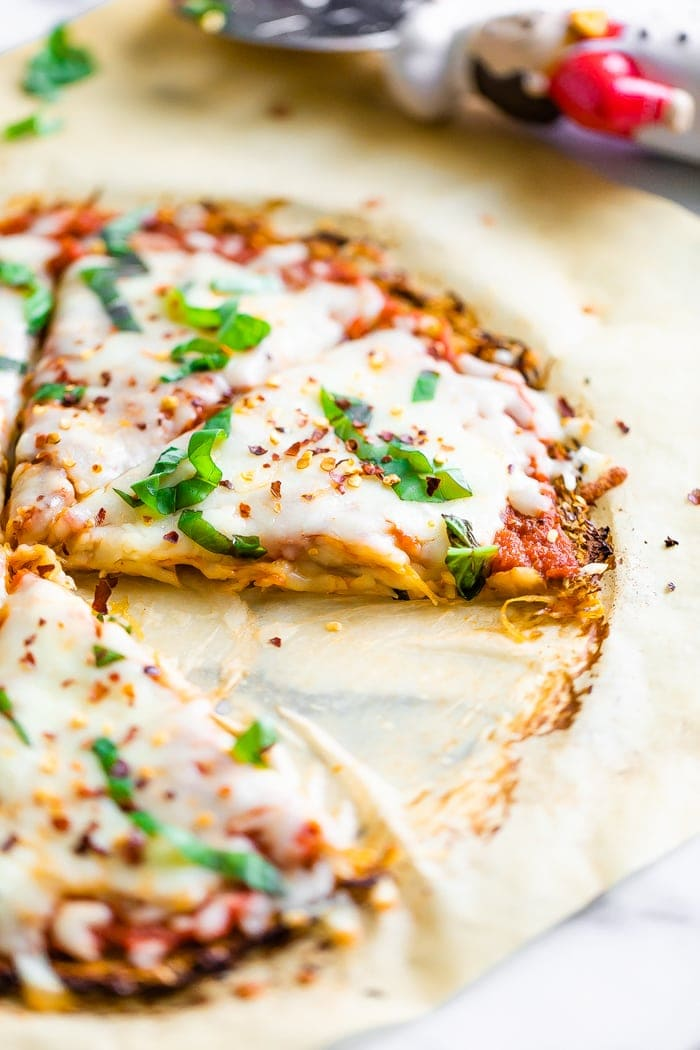 Esparguete de abóbora com crosta de pizza coberta com manjericão fresco e queijo. Uma fatia é cortada da pizza.
