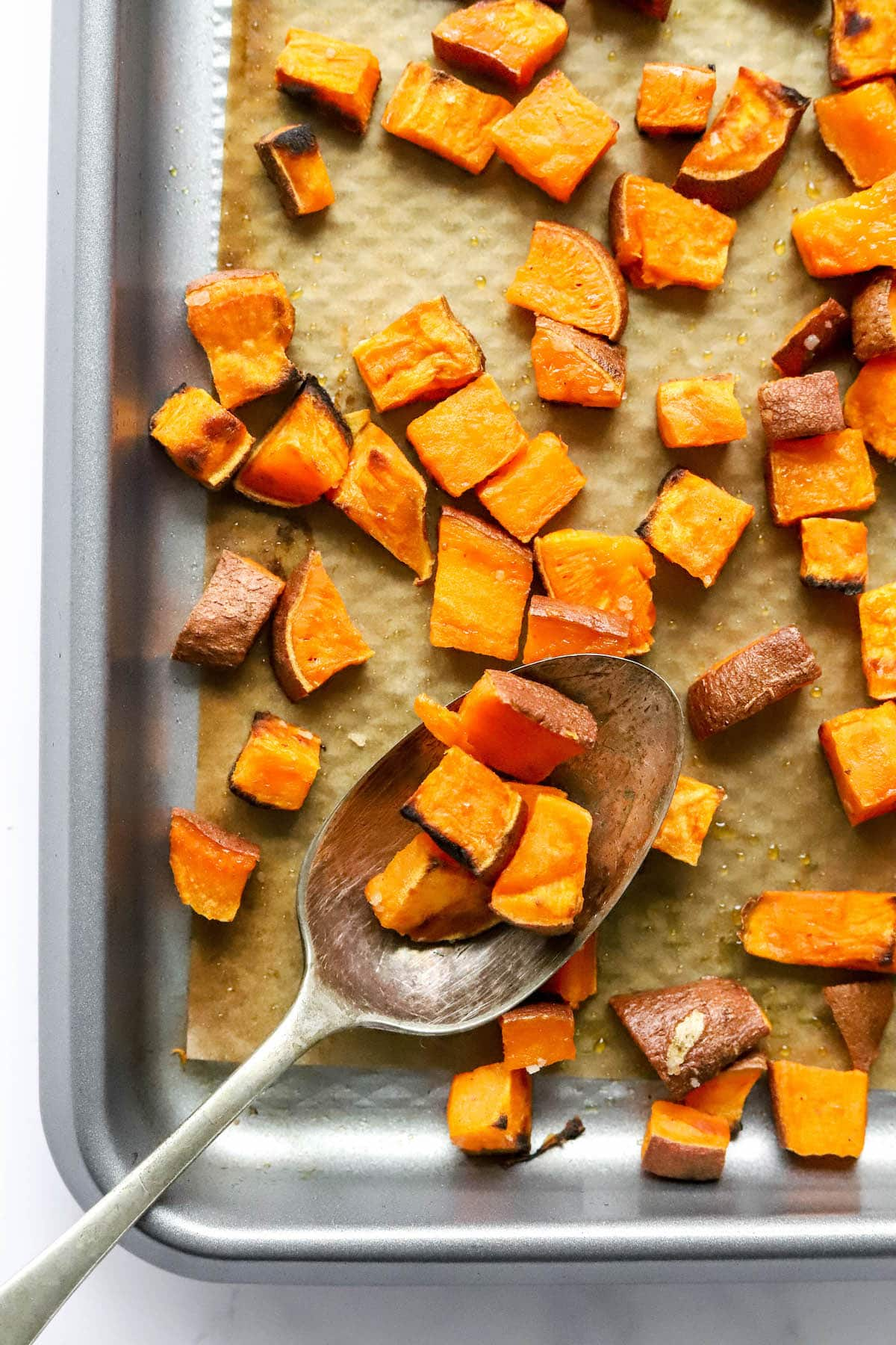 Uma frigideira de croutons de batata-doce, uma colher para servir repousa sobre a frigideira com alguns croutons sobre ela.