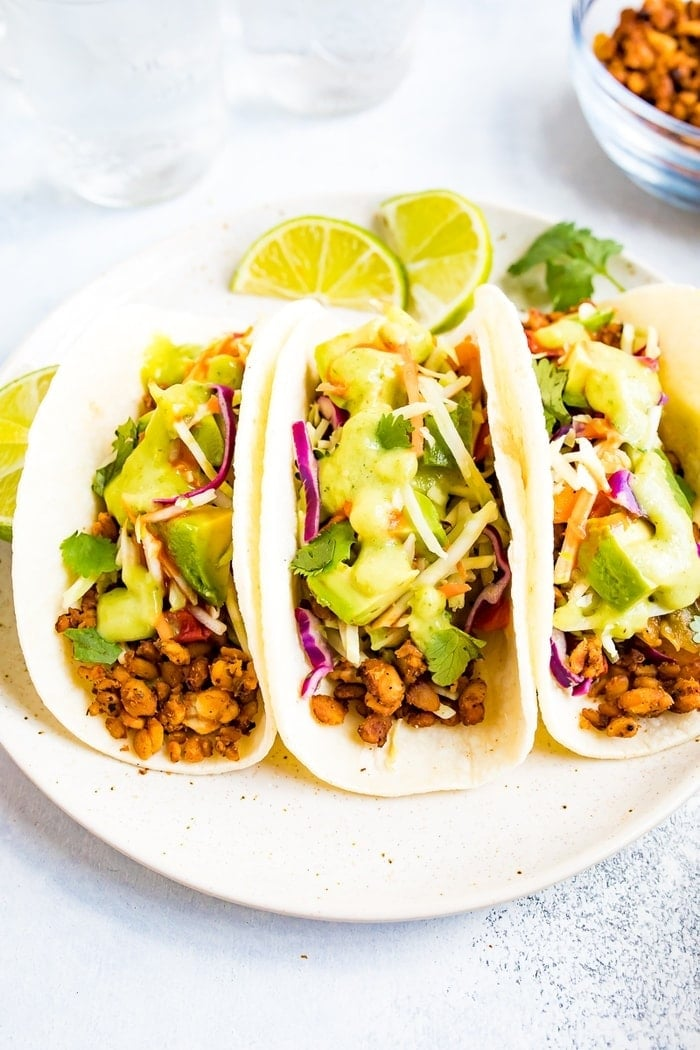 Três tacos tempeh com molho de abacate e tomatillo em um prato.