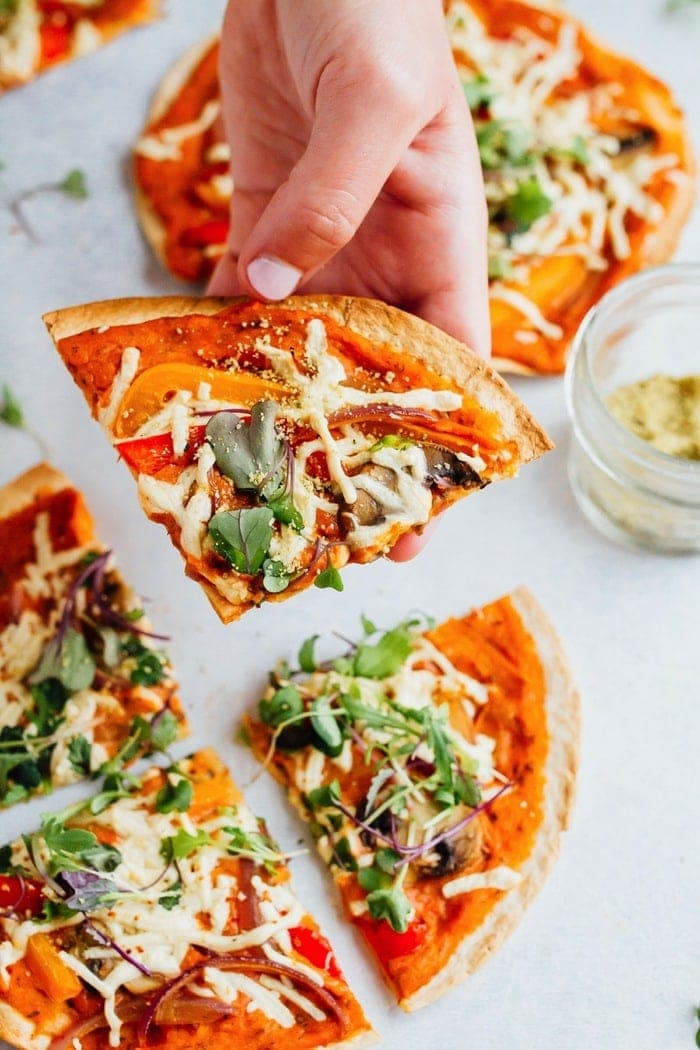 Pizza de hummus tortilla vegan com pimentas, verduras, cogumelos e queijo vegan.