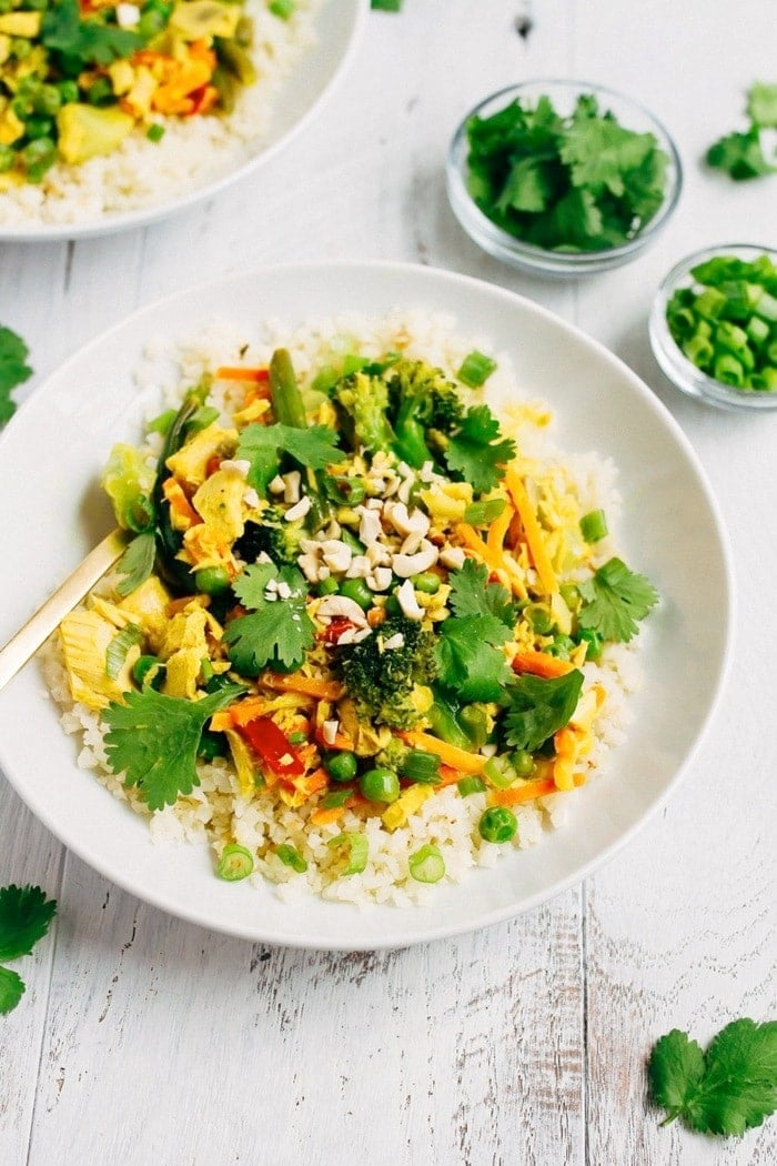 Caril de atum com legumes sobre arroz de couve-flor numa tigela branca, com pequenas tigelas de coentro e cebolinha verde na lateral.